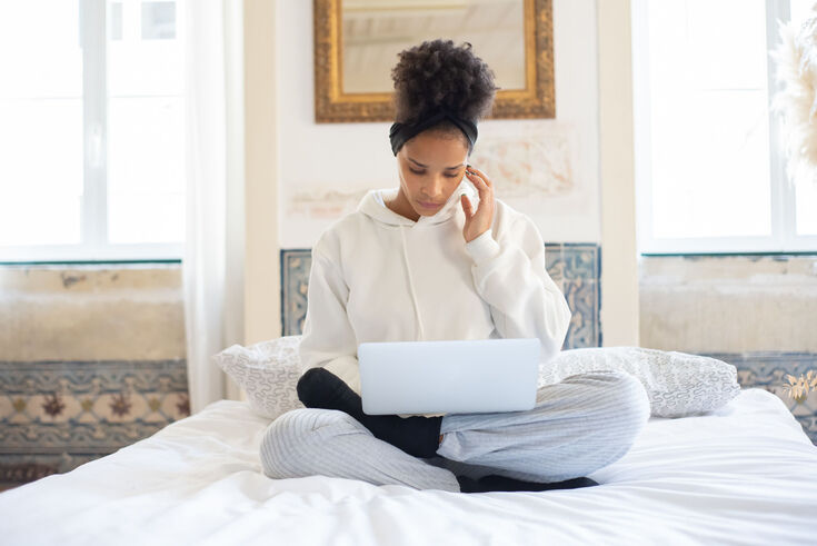 Woman sitting cross-legged on a white bed researching on a laptop