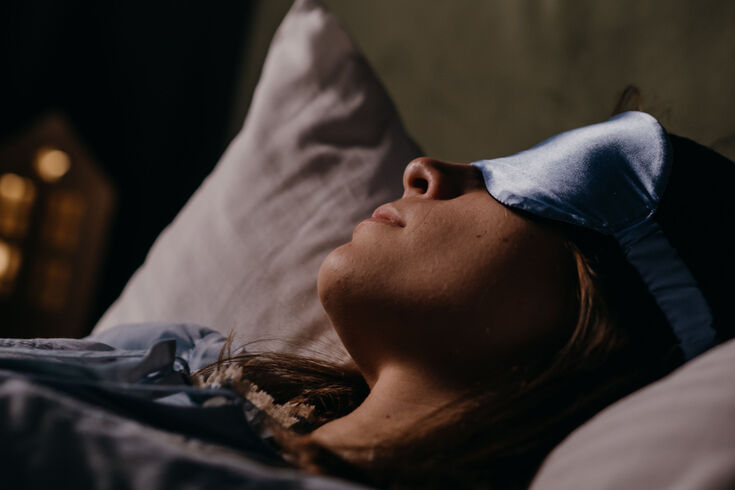 Woman lying on her back on a grey pillow with a sleep mask pushed up on her forehead