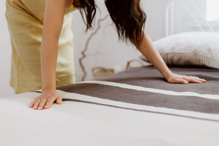 Woman smoothing a striped blanket flat across a freshly made bed
