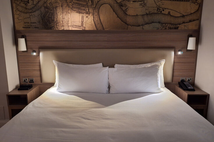 Hotel bed made up with crisp white bedding pulled taut across a firm mattress
