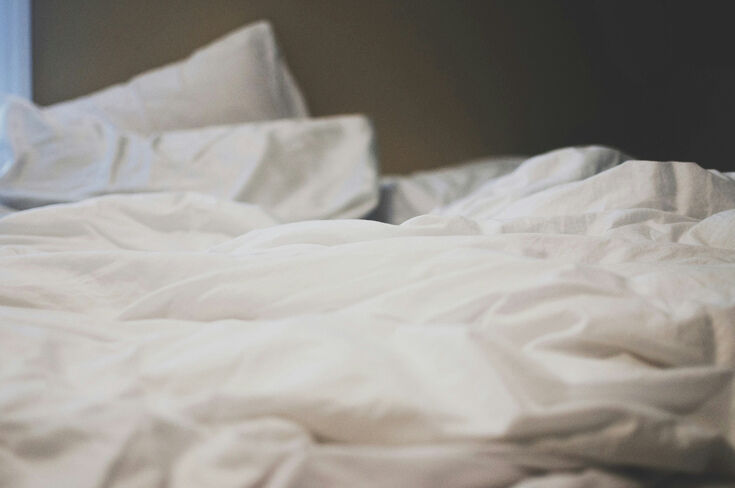 Unmade bed with white bedding pushed into folds after a night of shifting positions