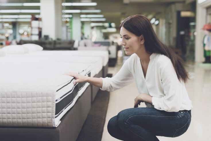 Woman kneeling to check the side panel and stitching of a mattress in a showroom