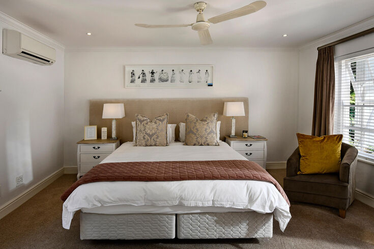 Neutral bedroom with a neatly made bed on a divan base, bedside lamps and a ceiling fan