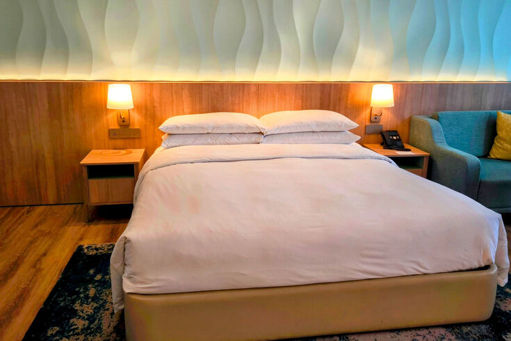 Hotel bed with smooth bedding drawn over the mattress under warm wall lamps